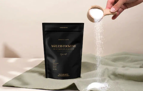 Energy metabolism booster powder from Ageless Cocktail being poured from wooden scoop beside black supplement pouch.