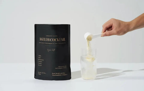 NMN drink supplement powder being poured into a glass of water next to Ageless Cocktail pouch