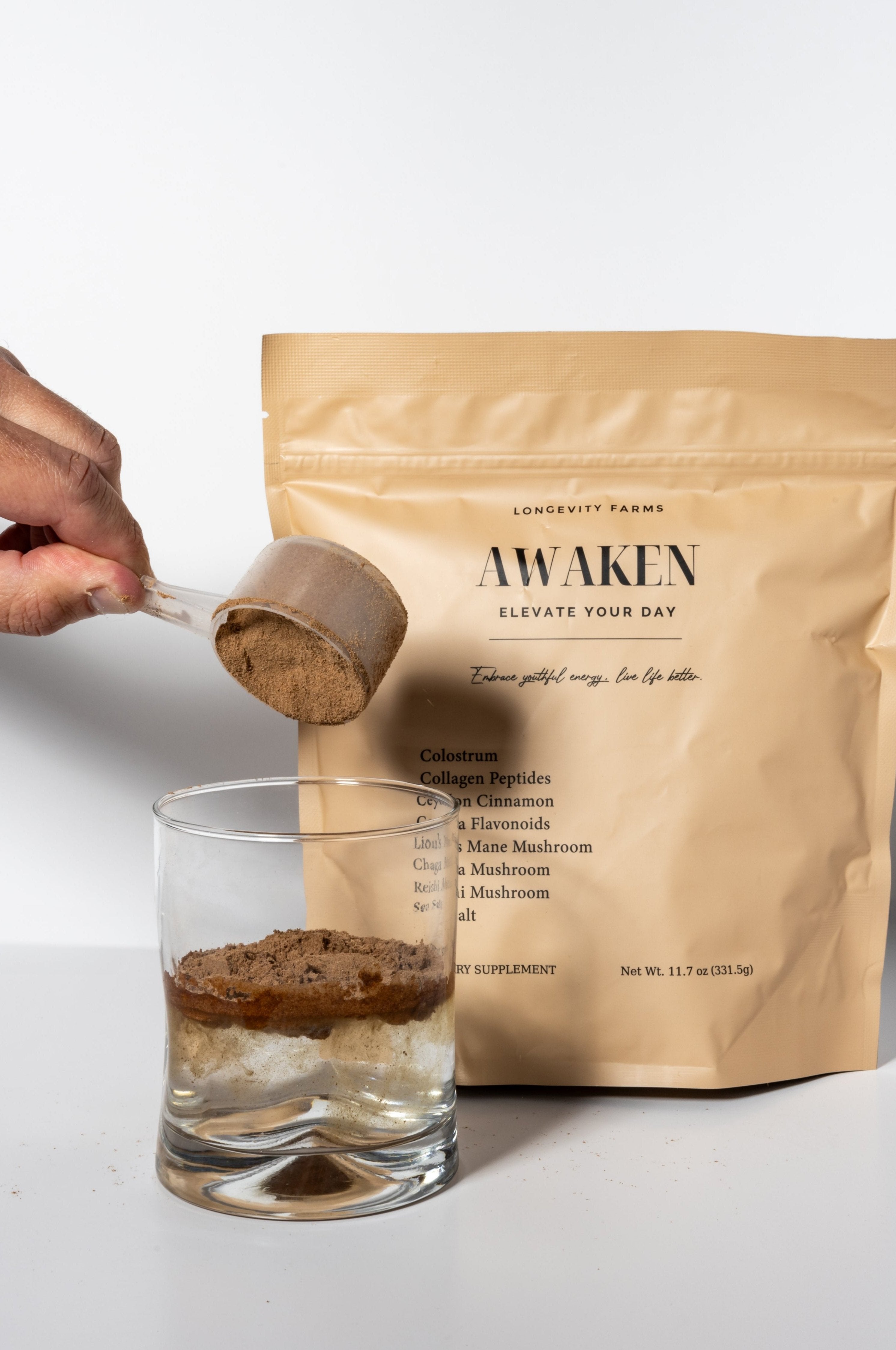 Longevity drink powder being scooped into a glass, with AWAKEN supplement bag featuring health-boosting ingredients in the background.