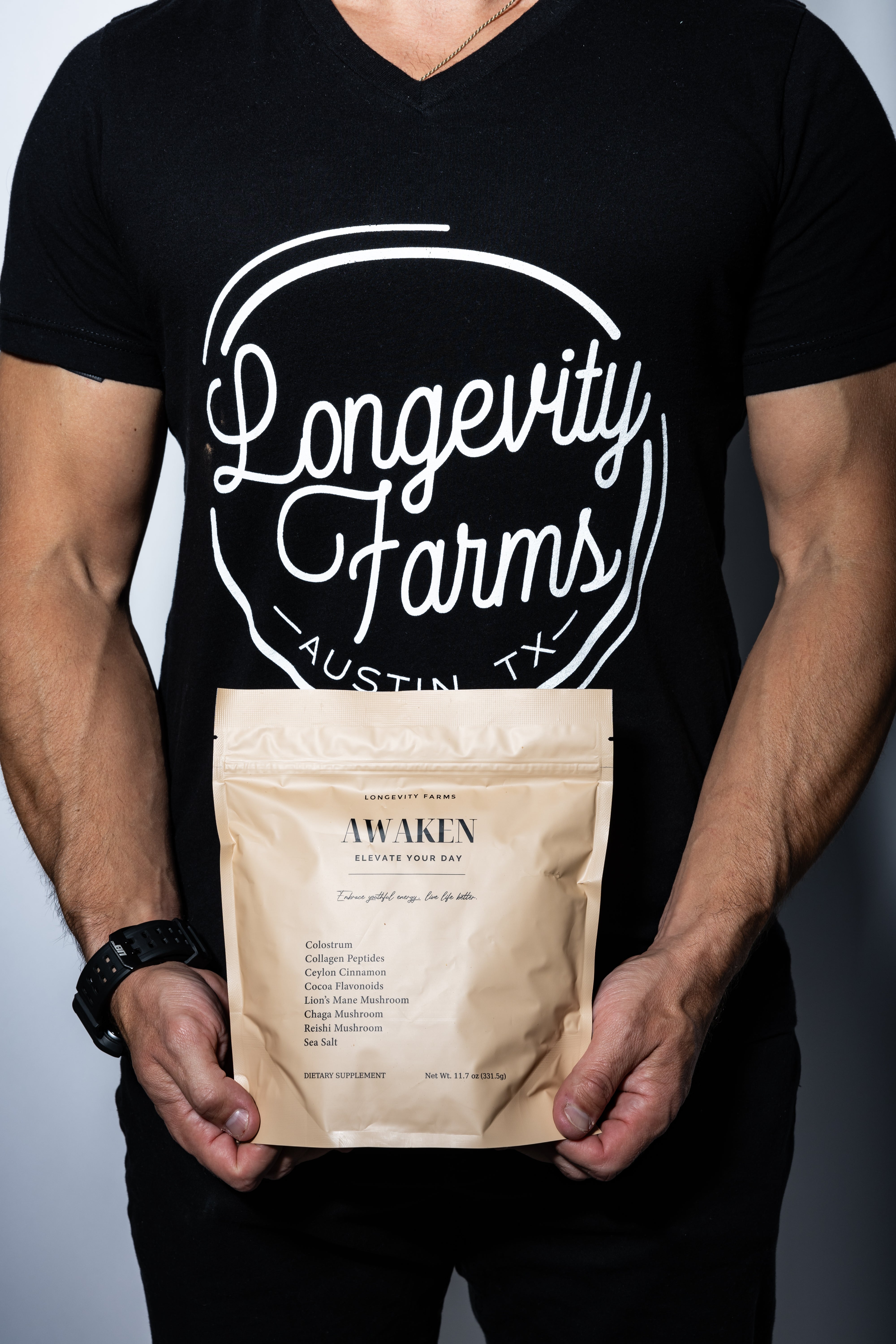 Collagen powder drink supplement called AWAKEN held by a person wearing a Longevity Farms t-shirt, featuring wellness-boosting ingredients.